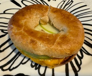 Apple and cheddar bagel on a black and white plastic plate.