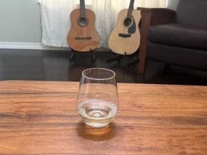 Glass of white wine on a coffee table with two guitars and a leather chair in the background.