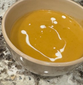Pumpkin soup in a beige bowl on a countertop. Drizzles of coconut milk are drizzled on top.