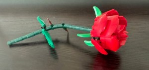 This photo shows a LEGO rose, resting on its side on a dark wooden table.