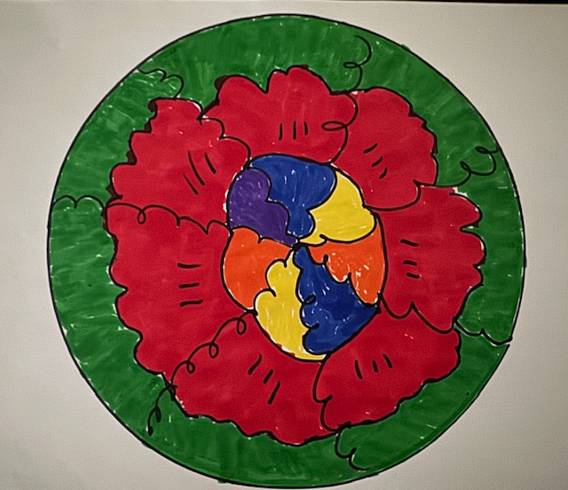 This photo shows a circular "mandala" with abstract shapes radiating from the center. The image is placed against a white background. The colors are bold: blue, yellow, purple, and orange in the center; red, then green around the rim.