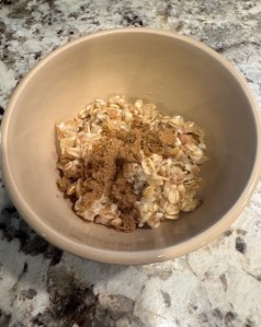 This photo shows a beige bowl, set on a marble-ish countertop. Inside the bowl, there is oatmeal, sprinkled with brown sugar.