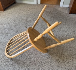 This image is a photo of a wooden chair, tipped over, upside down, on the floor, which is carpeted.