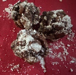 This photo shows three rum balls covered in powdered sugar and resting on a red napkin.