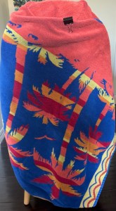 Brightly colored towel with palm tree pattern draped artistically over a chair and wrapped together/held by a binder clip
