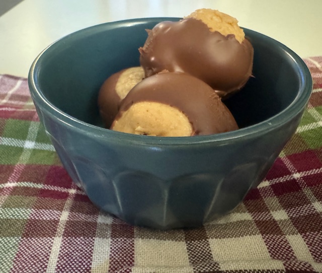 This photo shows a small ceramic bowl of candy buckeyes on a gingham striped napkin on a white table.