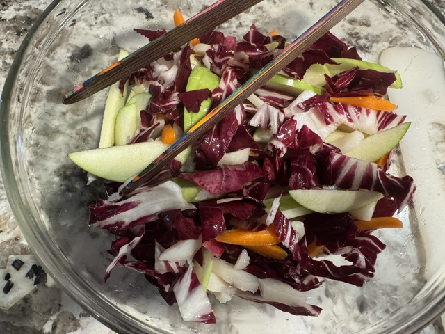 This is a photo of a salad in a clear bowl. The salad contains Granny Smith apple slices with the green peel still on, radicchio leaves, thinly sliced carrots, and sliced water chestnuts.