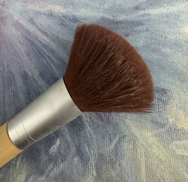 This is a picture of a makeup brush against a swirled muted blue, painted background.