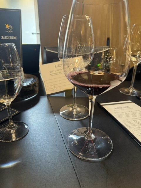 This picture shows clear wine glasses set on a black countertop, with a Northstar sign/menu in the background. One of the wine glasses has a splash of red wine in it.